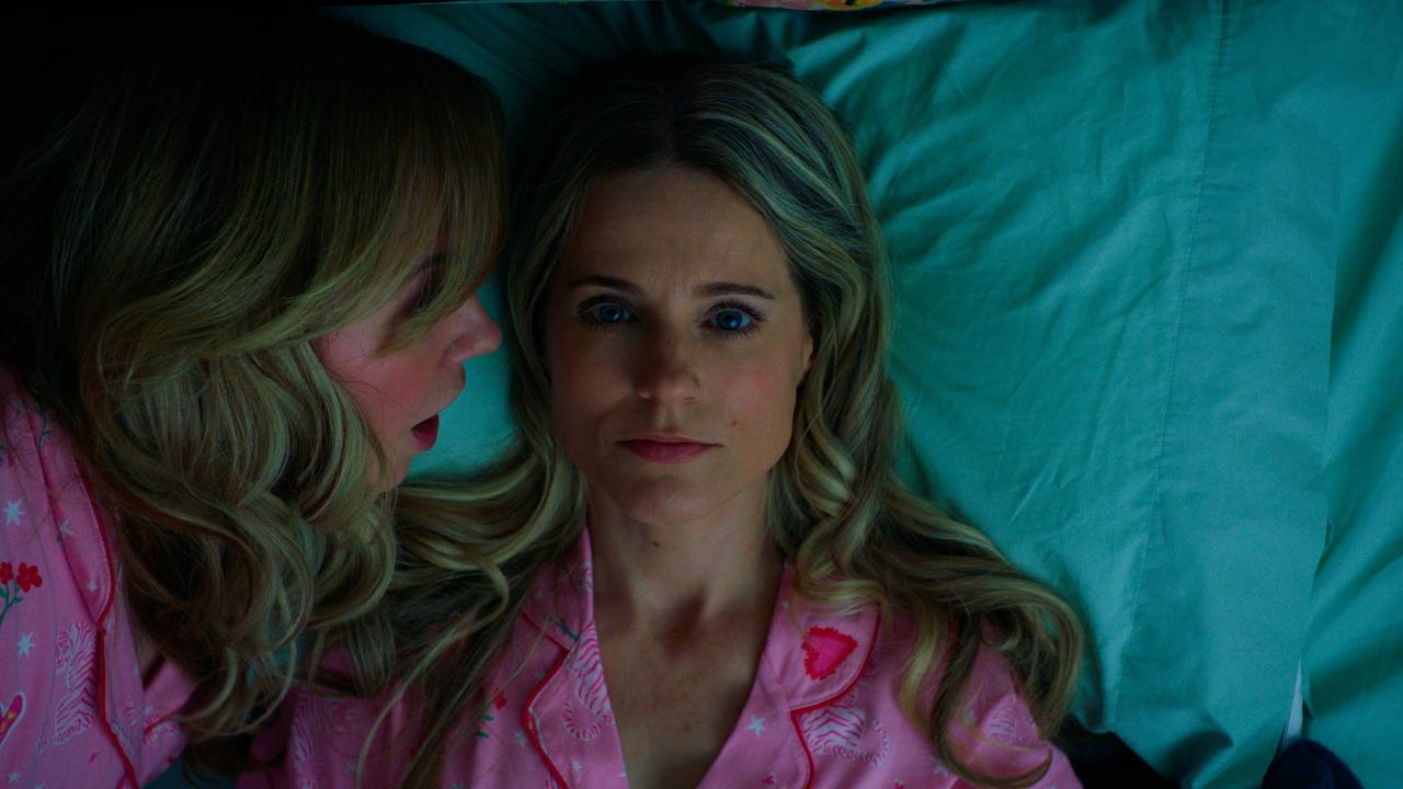 A woman whispers beside another lying awake on a teal pillow.